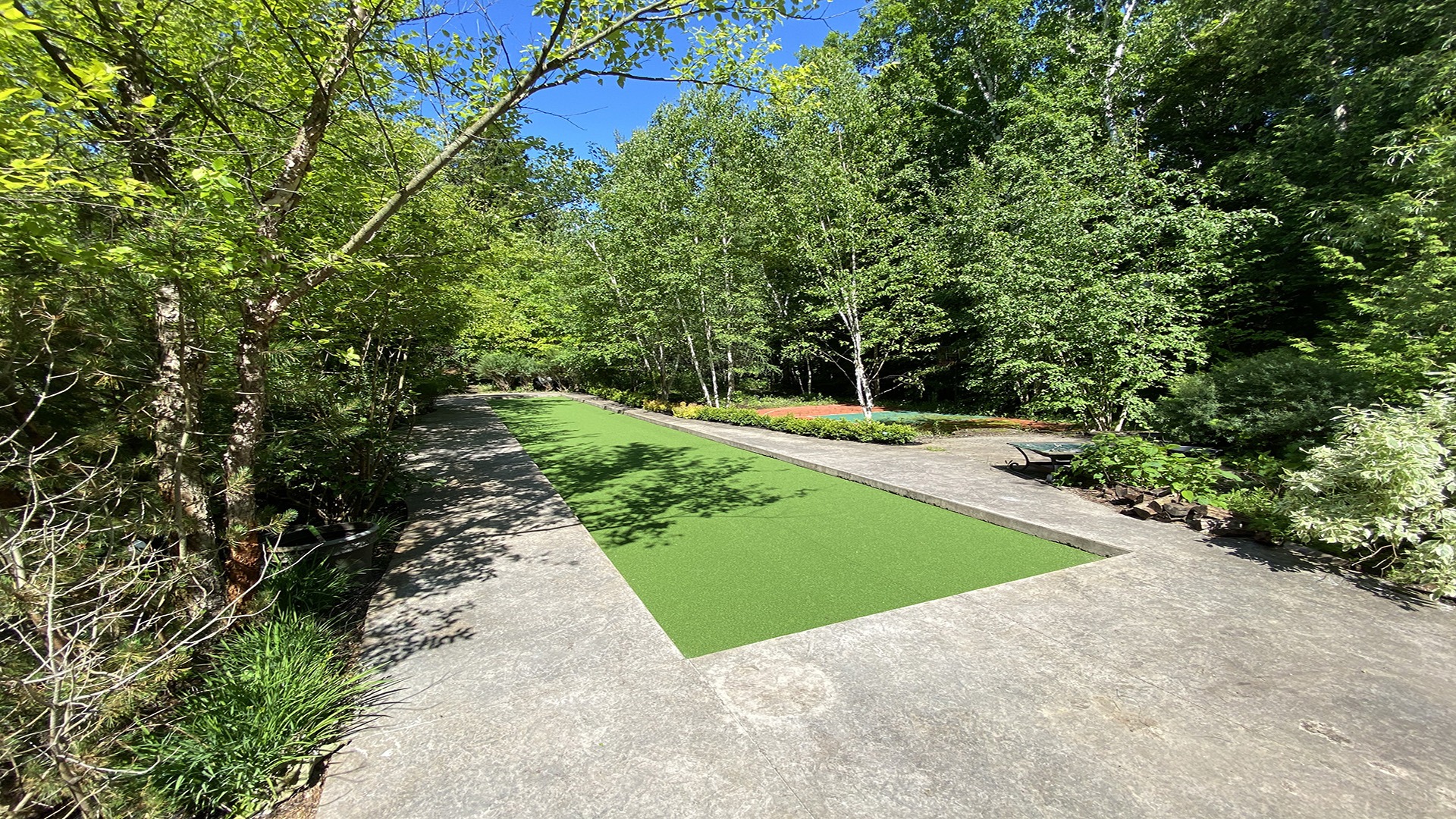 A lush garden features a rectangular green area surrounded by trees and pathways under a clear blue sky.