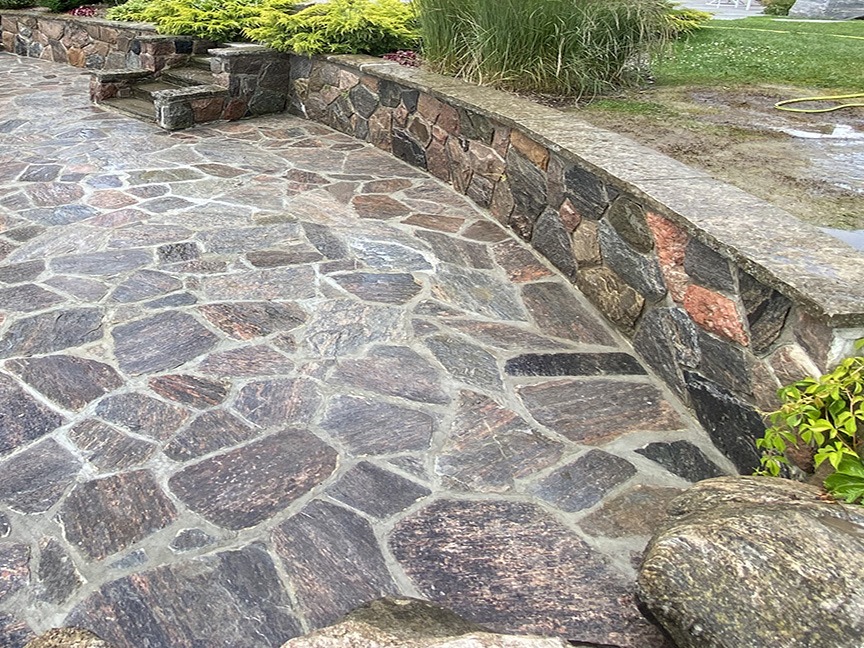 Stone patio with intricate pattern, surrounded by rock walls and lush greenery. A peaceful outdoor setting, suitable for relaxation or gatherings.
