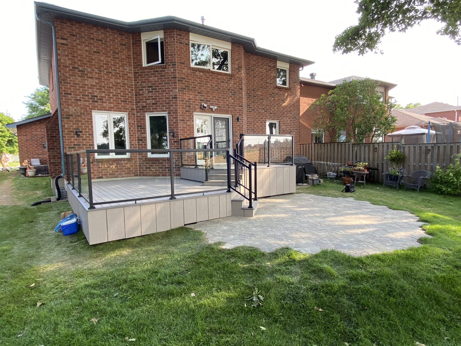 Brick house with a fenced wooden patio and green yard, featuring outdoor seating and a grill. No landmarks or historical buildings visible.