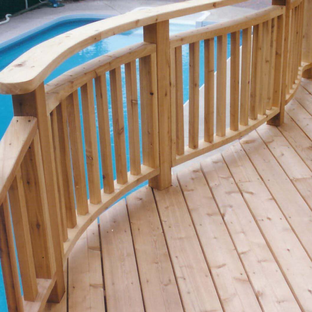 Wooden deck with curved railing overlooks a clear blue swimming pool. The deck's light wood complements the inviting pool setting. No people visible.