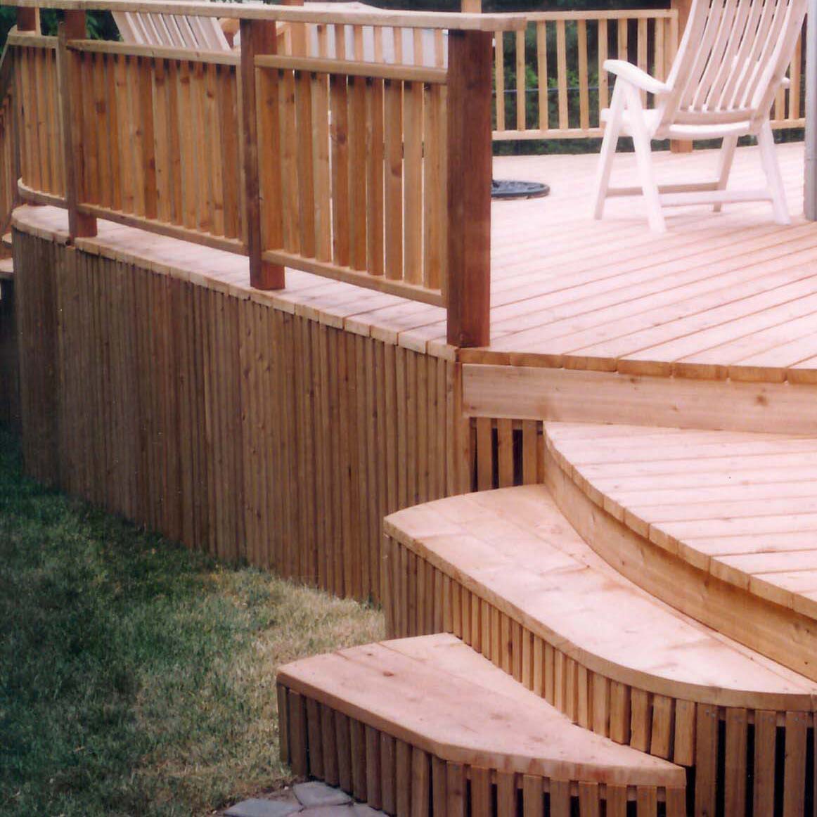 A wooden deck with curved steps, featuring two white chairs on top. The structure is surrounded by grass and landscaped garden area.