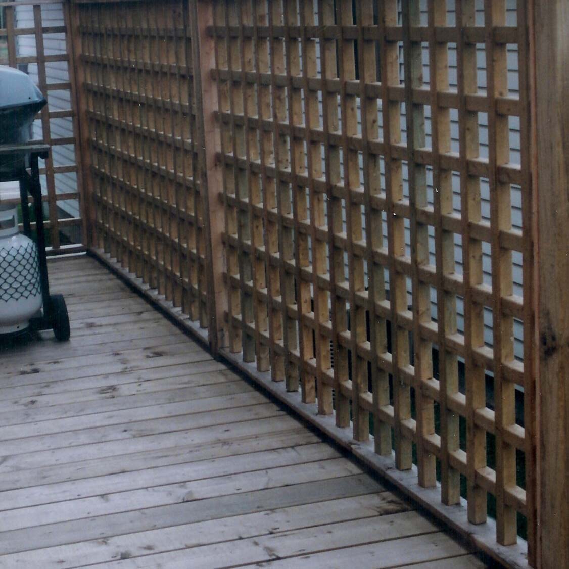 A wooden deck with lattice fencing and a gas grill. The area appears to be a backyard or outdoor patio space.