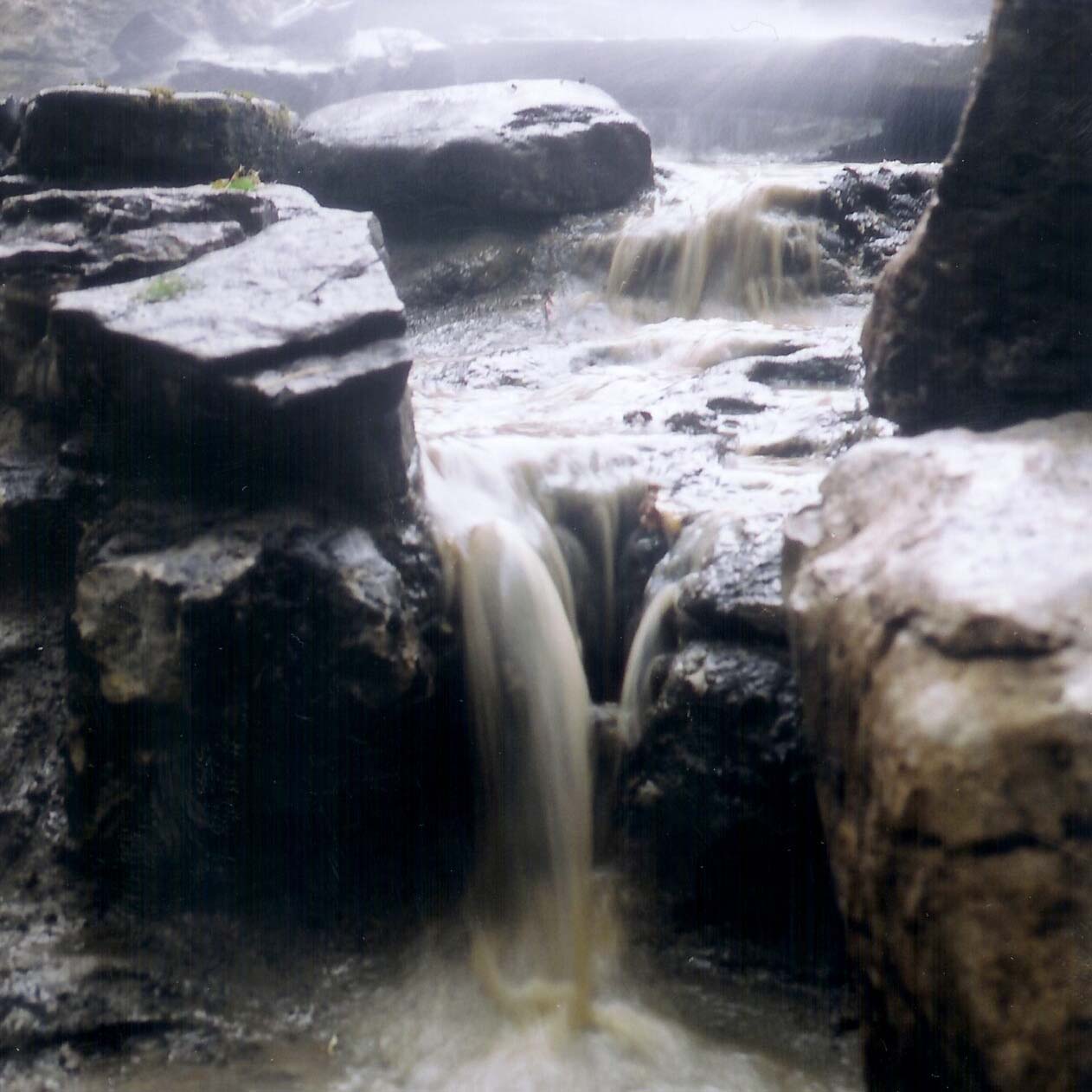 Small waterfall cascading over moss-covered rocks in a misty forest setting, creating a serene, natural atmosphere with flowing water.