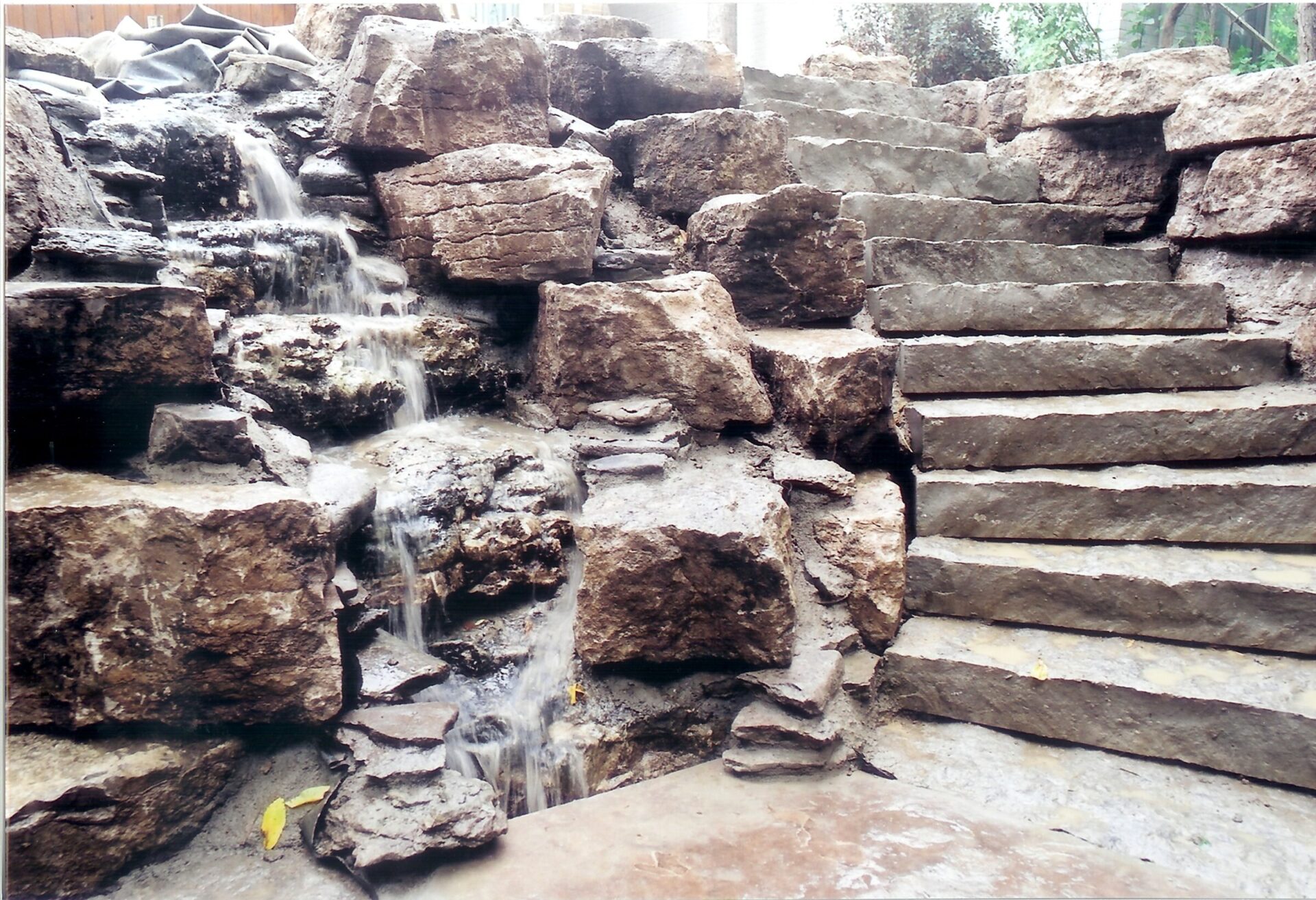 Stone staircase beside a rocky waterfall, with water cascading down multiple levels. Natural setting with no visible people or landmarks.