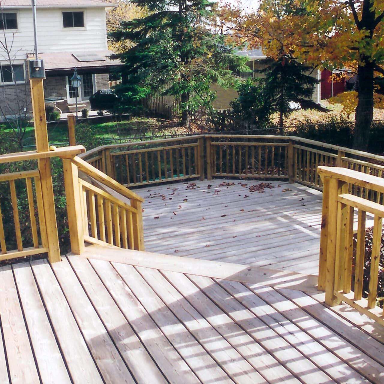 A wooden deck with steps leads to a backyard surrounded by trees. A house is visible, with autumn leaves scattered around.